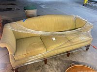 Front view of light olive camelback sofa wrapped in plastic