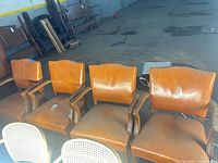 Four caramel vinyl armchairs lined up showing fronts
