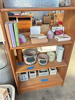 Wood shelf holding planters, pots, vases, agate bookends, books and boxed sketch set