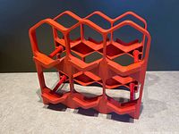 Overall view of red modular plastic wine rack showing front and side hexagonal bottle openings