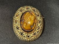 Front view of oval Florenza gold-tone filigree brooch with amber cameo