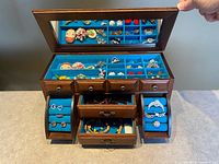 Open jewelry box showing mirror, teal velvet compartments, side ring rolls, drawers, assorted jewelry pieces