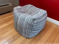 Woven square pouf ottoman on hardwood floor showing full shape, fabric texture and colours