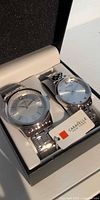 Both wristwatches in open presentation box with hang tag visible