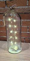 Full view of glass bottle decorative light with LEDs illuminated and rope bow