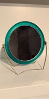 Front view of teal round tabletop mirror on metal stand