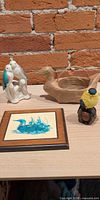 all four items grouped on tabletop: ceramic bird pair, duck basket, framed loon tile, resin goldfinch