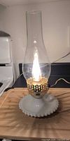 Lamp illuminated showing milk glass base, brass collar, clear chimney