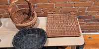Three baskets on table: round handled basket, dark oval basket, flat square basket