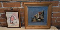 Needlepoint and placard side by side against brick wall