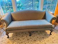 Front view of full three-seat sofa showing upholstery pattern, backrest shape, and all four carved legs