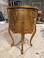 Front view of one gold rococo drum end table showing carved drawer and cabriole legs