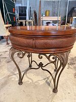 Full view of oval side table showing wood top, rattan apron, metal legs