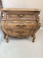 Front view of light oak French Provincial nightstand showing four drawers, ornate carvings, brass-tone pulls
