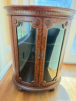 Front view showing burl veneer finish, curved glass doors, brass-tone hardware, bun feet