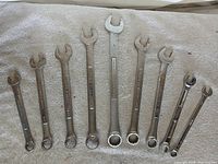 Nine combination wrenches laid out on cloth, showing both open and box ends