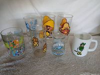 Seven assorted cartoon character glasses and mug displayed together