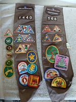 Both brown Girl Scouts sashes laid out showing troop numbers, council tab and numerous patches