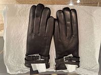 Black leather gloves laid flat showing front side and buckle details