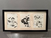 Full view of framed artwork showing three ink panels side by side in black frame