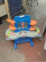 Front view of Step2 race track playset showing blue tower, orange ramps, silver tabletop track on blue stand