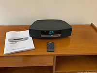 Front view of Bose Wave Music System, remote, and manual on wood surface