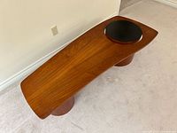 Full view of teak coffee table showing elongated shape, black circular inset, pedestal bases