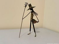 Front view of metal figurine, hat, staff, patina visible