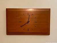 Front view of rectangular wood wall clock showing dial and markers