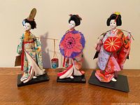 All three geisha dolls standing on black bases against neutral background