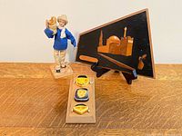 All three items displayed: marquetry plaque on easel, Sabra doll, triple-face plaque