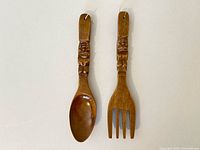 Front view of spoon and fork showing carved tiki handles and utensil heads