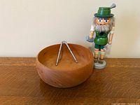 Wood bowl with metal tongs resting inside and Bavarian nutcracker figure standing beside