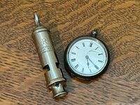 Whistle and pocket watch side by side on wood surface