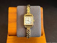 Front view of watch on stand showing full bracelet and square dial