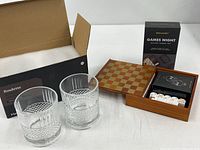 Both glasses beside open Games Night wood box showing checkerboard lid and interior contents, original packaging visible