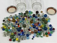 Both empty jars with lids and large pile of assorted glass marbles displayed