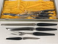 Open presentation box showing six steak knives in sleeves and three carving pieces laid out