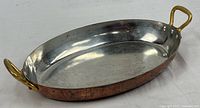 Full view of oval copper gratin pan showing copper exterior, stainless interior, brass handles