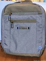 Front of blue NextTech crossbody bag showing zippers, logo plate, condition