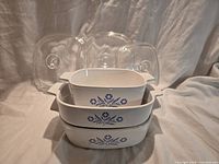 Three Corning Ware Blue Cornflower square dishes stacked with three glass lids behind