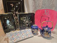Lot overview showing black floral trays, white floral sushi tray, red plate, blue ginger jar and teapot
