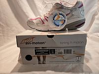 Side view of sneaker on top of original box with hang tag showing style number and size