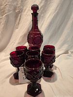 Full view of Avon Cape Cod cranberry decanter with stopper and surrounding cordial glasses