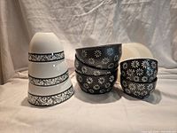 Stacked white bowls with scroll band, stacked black bowls with flower pattern and lid behind