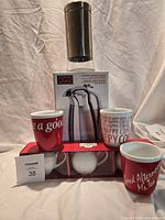 Group shot showing boxed Oggi carafe, three red Bodum mugs, stainless steel/glass canister, and boxed set of three white pitchers