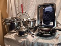 Overall view of stainless cookware, non-stick pans, colander, utensil caddy, baking pan, packaged kitchen textile set and accessories