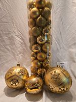 Tube of small gold ornaments and three oversized jeweled gold ornaments placed in front