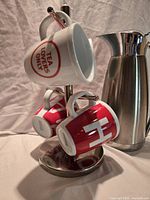 Oggi carafe, stainless steel mug rack holding four red and white Bodum mugs