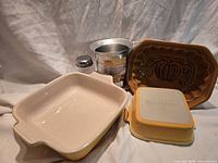 All five items grouped: two yellow Le Creuset pans, brown Crate & Barrel loaf pan, aluminum measuring cup, stainless shaker